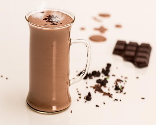 Traditional clay pot with steaming cacao beverage next to a wooden whisk