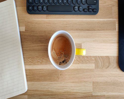 A wooden desk with a notebook and a cup of cacao indicating a workspace